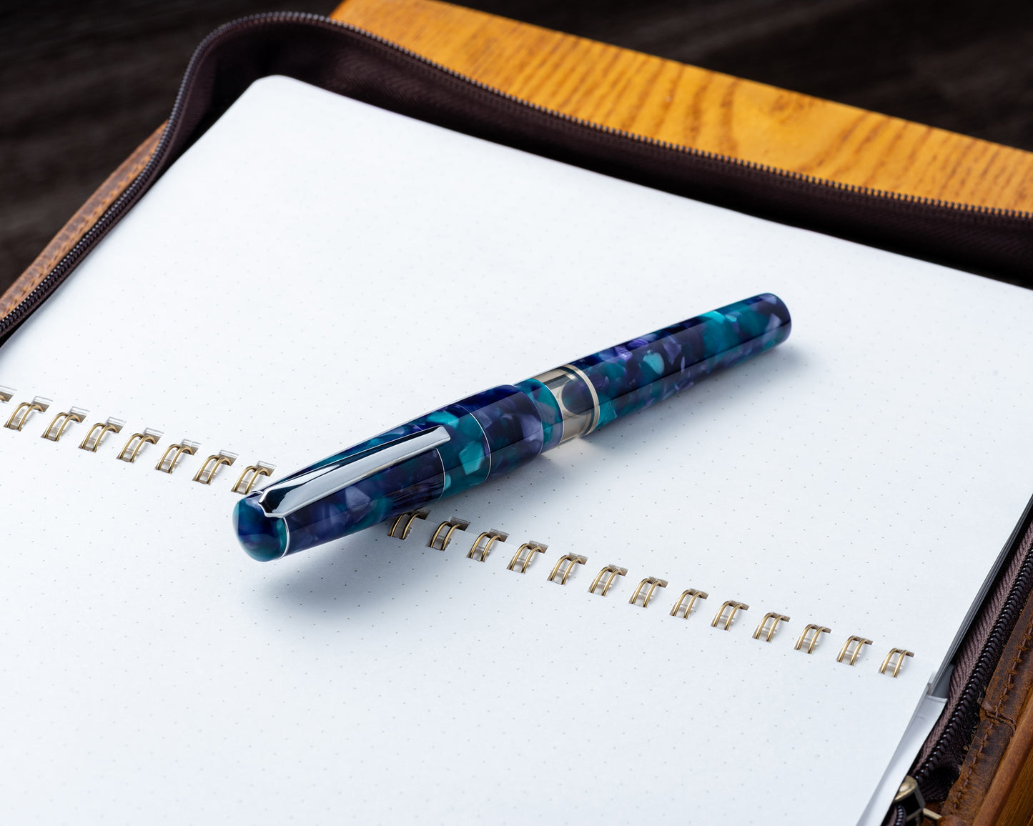 Blue and silver pen on a white notebook with a wooden cover